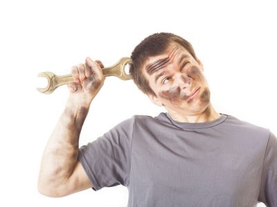 man with grease on face and body holding a wrench with a quizzical expression
